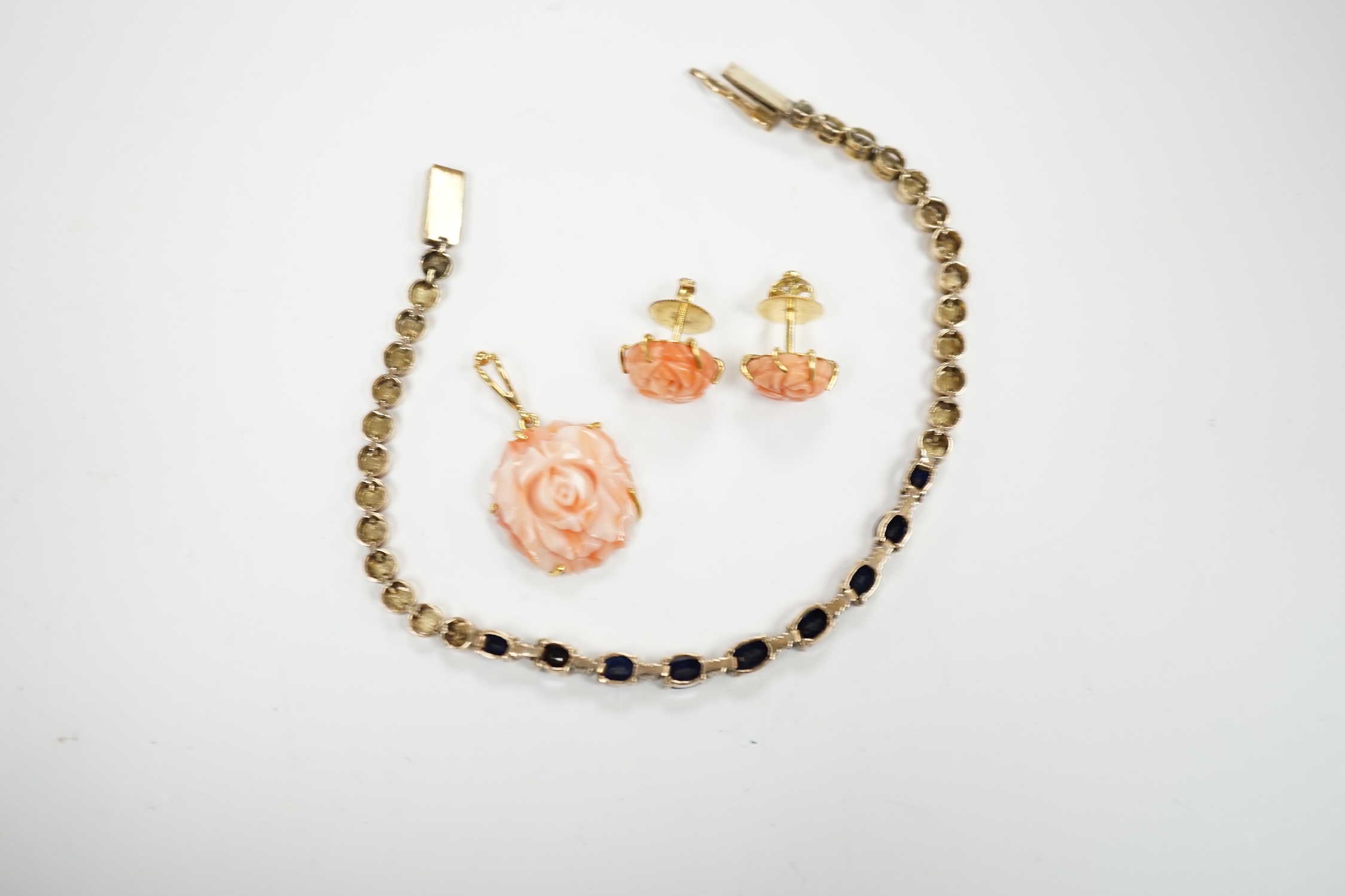 A modern 18ct and carved coral set 'rose' pendant, 16mm and a pair of matching ear studs and a yellow metal and two colour sapphire set line bracelet, 18cm.